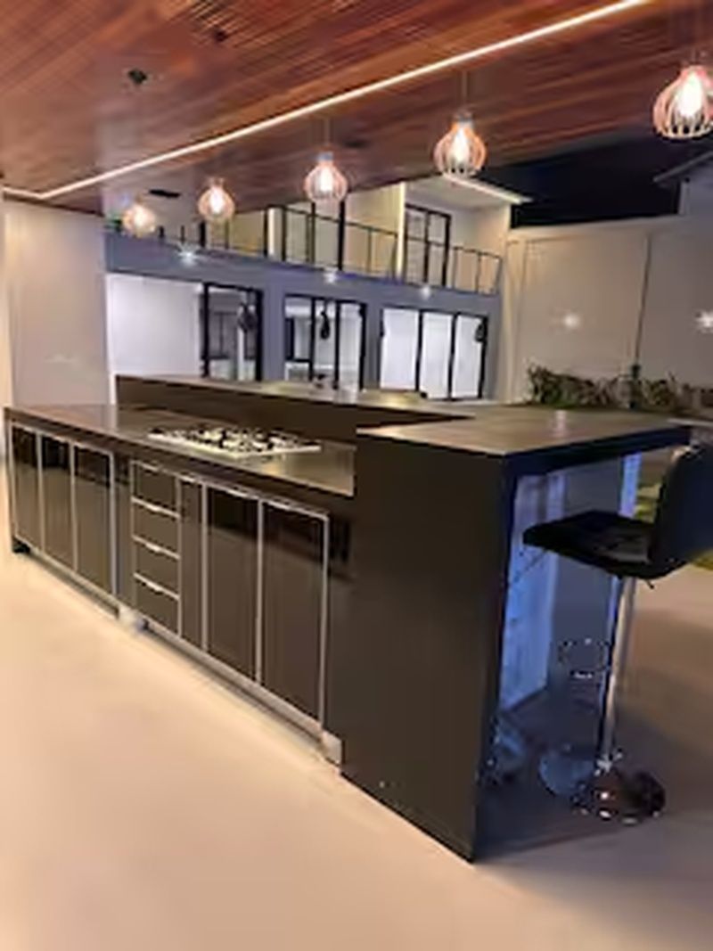 Una cocina moderna con una isla central, taburetes de bar, iluminación colgante y techo de madera.