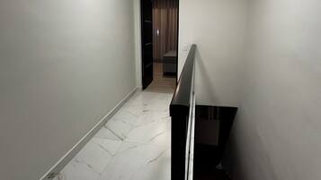 Um corredor com piso de mármore branco, escada de madeira e uma porta que dá para um quarto com cortina.