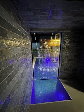 A modern indoor pool area with a water feature and illuminated walls.