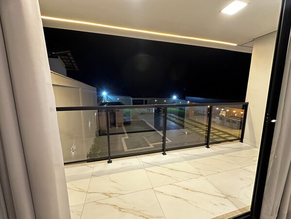 A balcony with a glass railing, a tiled floor, and a view of a building with lights at night.