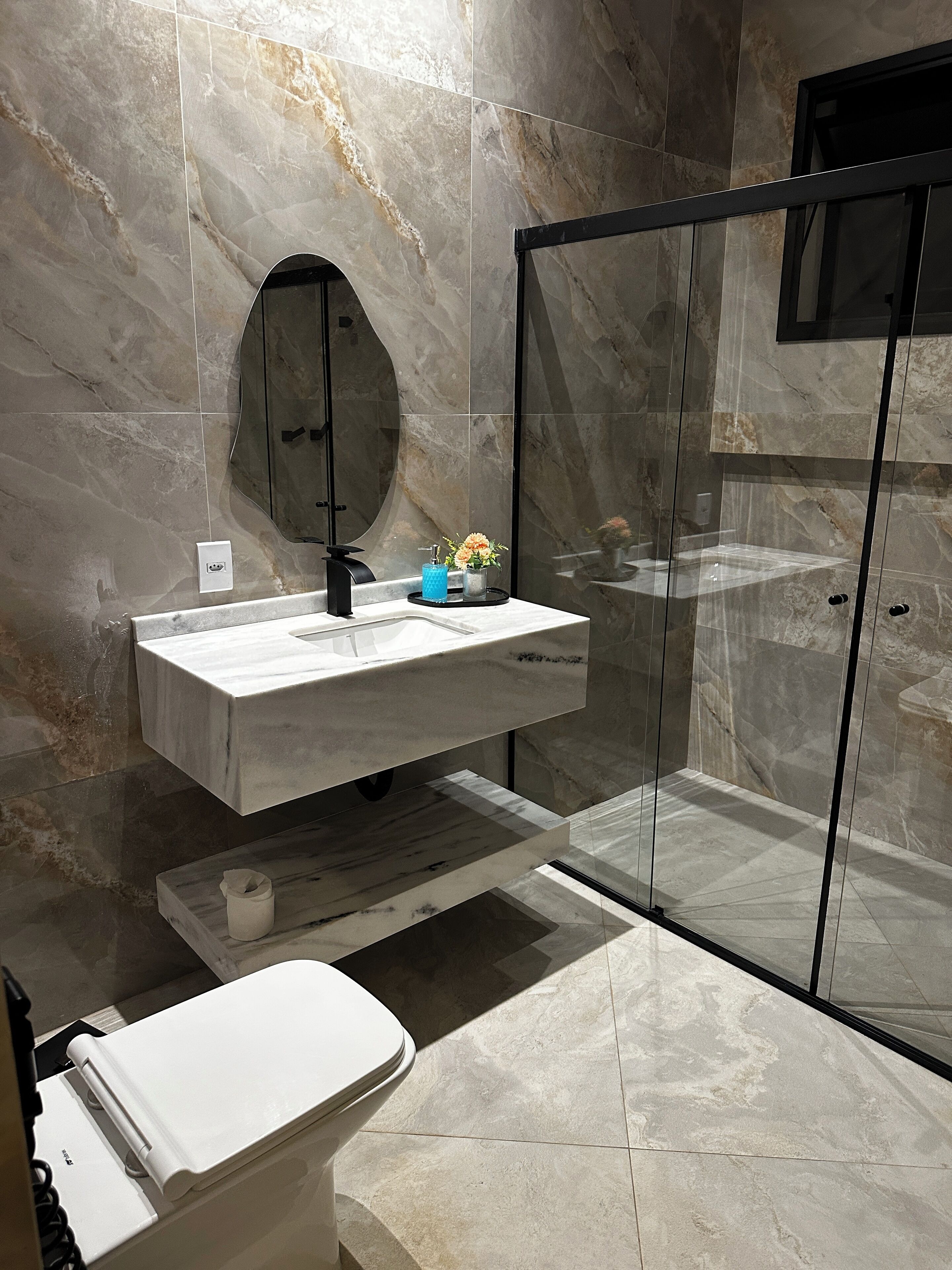 Ein modernes Badezimmer mit Marmorwaschtisch, einer Glasdusche und einer Toilette.