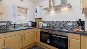 A compact kitchen with a gas stove, microwave, oven, and a window with blinds. - The residency rooms liverpool  (Liverpool)
