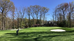 En golfbana med en sandbunker, träd och en byggnad i bakgrunden.