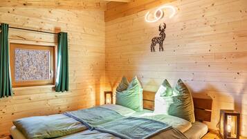 A wooden cabin bedroom with a bed, pillows, a window with curtains, a wall-mounted light, and a decorative animal silhouette.