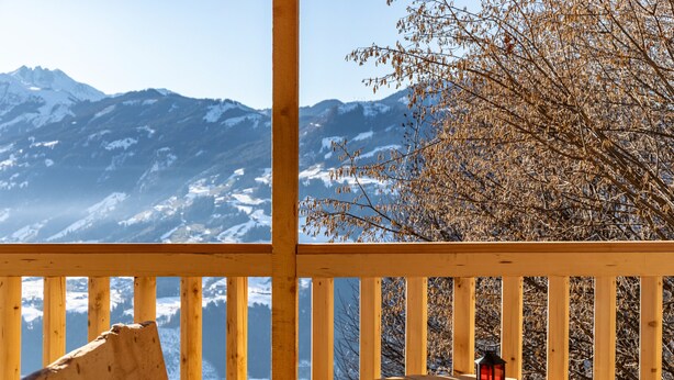 Uma varanda de madeira com uma mesa, duas lanternas e vista para montanhas cobertas de neve.