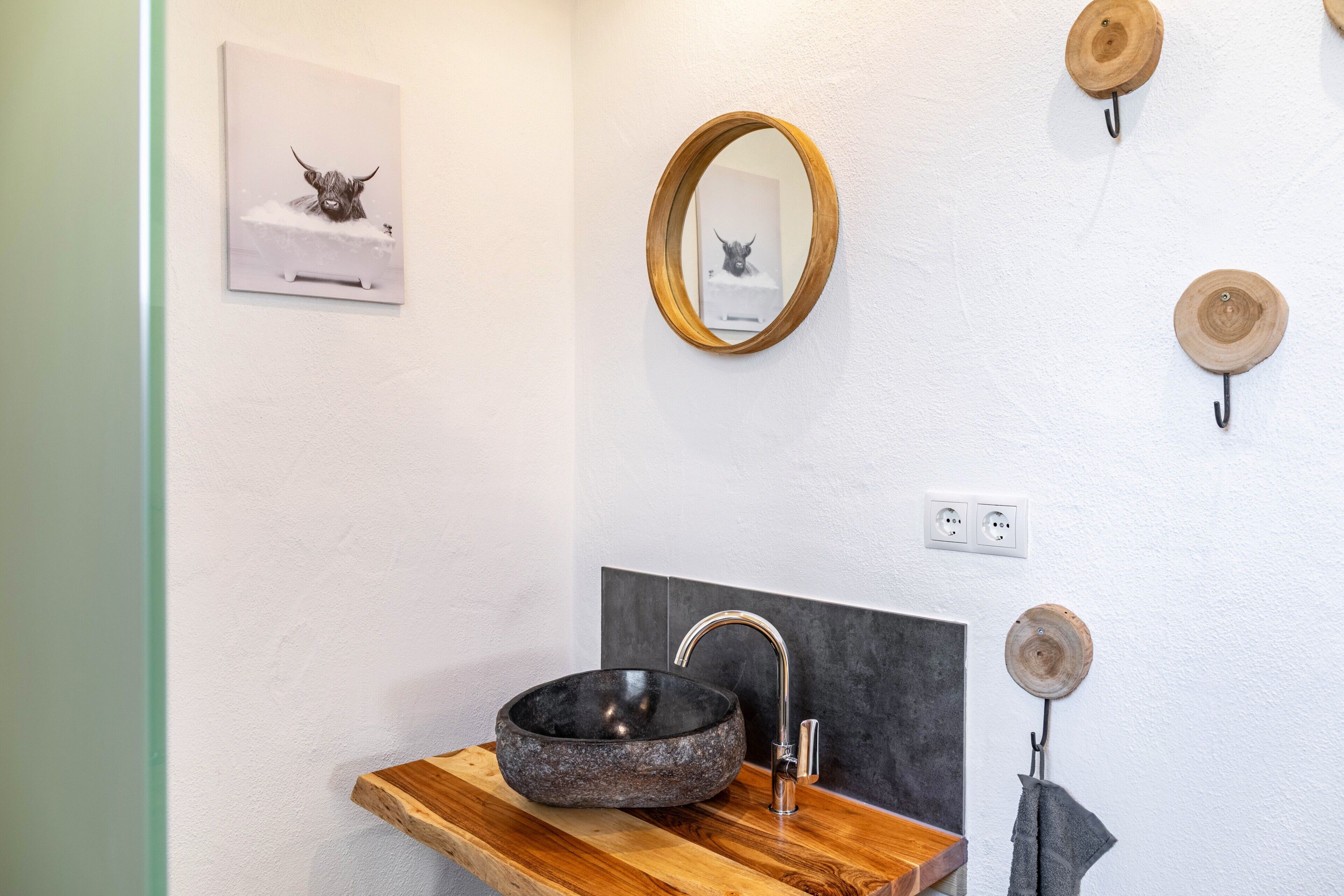 Une salle de bain avec un lavabo en pierre, une étagère en bois, un miroir et des décorations en bois fixées au mur.