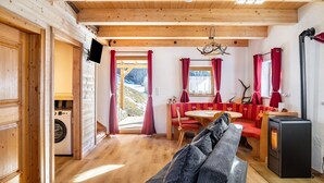 Interior acolhedor de uma cabana com paredes de madeira, área de jantar, sofá, máquina de lavar e lareira.