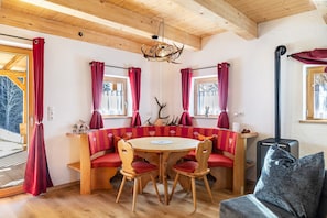 A wooden interior with a round table, red upholstered seating, and a fireplace.