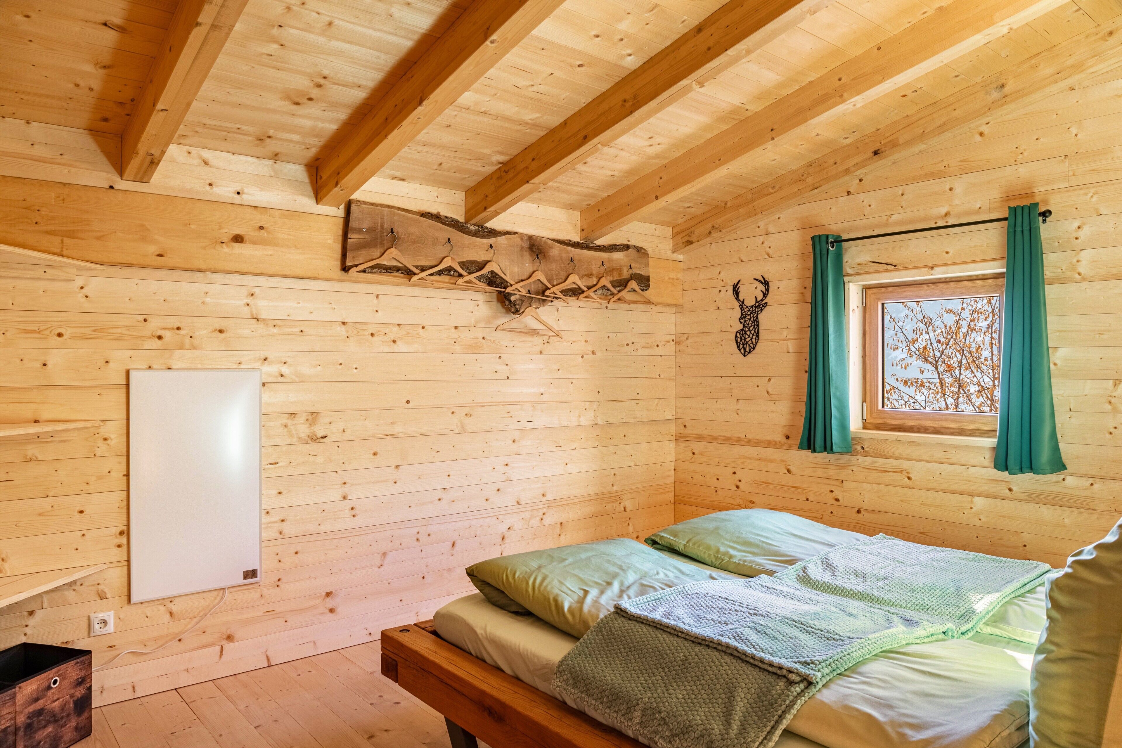 Een houten kamer met een bed, een raam met gordijnen en een wandradiator.