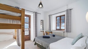 Une chambre avec un lit superposé, un lit simple, un radiateur, une fenêtre avec des rideaux et un luminaire suspendu.