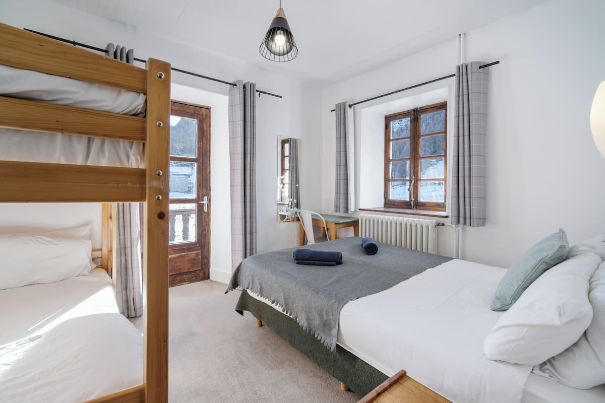 Un dormitorio con una litera, una cama individual, un radiador, una ventana con cortinas y una lámpara colgante.