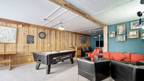 Une table de billard, un jeu de fléchettes et des queues de billard se trouvent dans une pièce aux murs en bois et dont un mur est peint dans une nuance de turquoise.