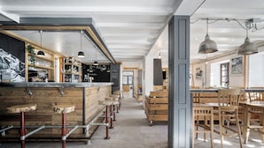 Un grand espace bar doté de tabourets en bois et d’un long comptoir, entouré de tables et de chaises en bois.