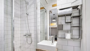 Une salle de bain moderne avec des murs recouverts de carreaux blancs, un meuble en bois sous le lavabo, une douche avec une porte en verre et une étagère en métal contenant des articles de toilette.