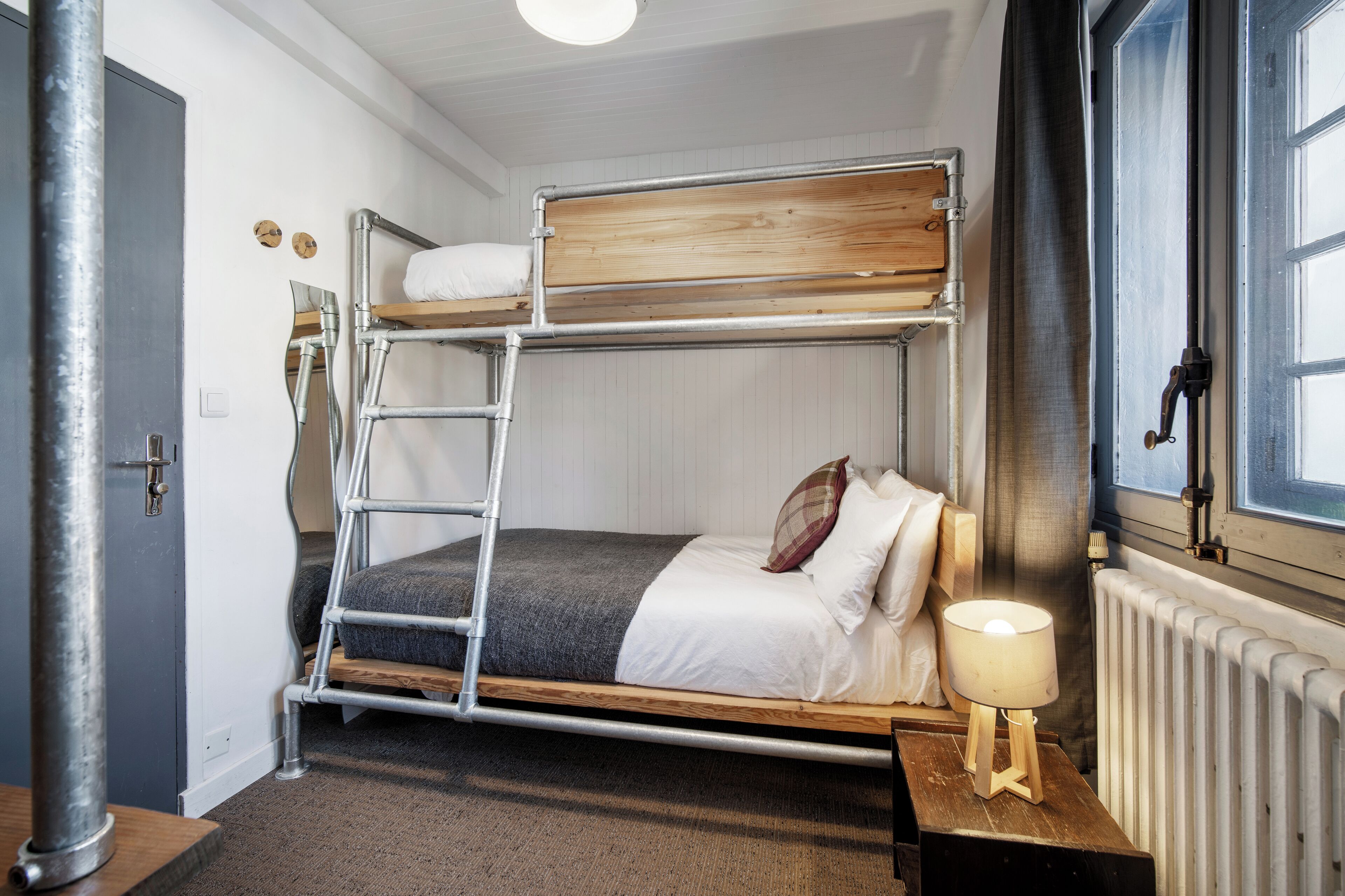 A bunk bed with a ladder, a bedside table with a lamp, and a window with curtains.