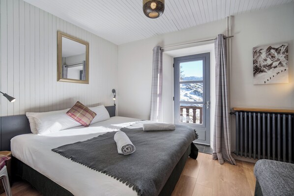 A bedroom with a bed, a window with curtains, a radiator, and a painting on the wall. - Chalet Auberge Les Mélèzes (Tignes)