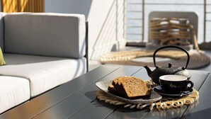 A deck with a table set for tea and bread, a sofa, and a view of the water. - Apartment 2 - El Classico Apartments (Rubavu)