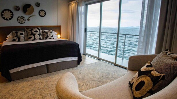Een slaapkamer met een bed, een sofa en een groot raam met uitzicht op zee.