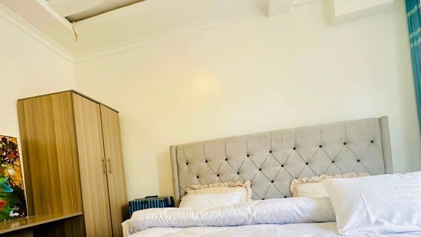 A bedroom with a large bed, a wooden wardrobe, and a tufted headboard. - Apartment 2 - El Classico Apartments (Rubavu)