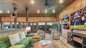 A modern interior with a green sofa, a round wooden coffee table, and a large TV screen displaying a football game. - 26 Guests | Resort Waterpark | Indoor Pool | Views (Sevierville)