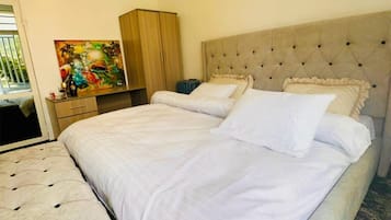A bedroom with a large bed, a chest of drawers, a painting, and a ceiling light.