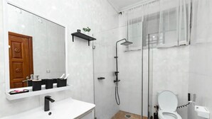 A modern bathroom with a white sink, a mirror, a shower, and a toilet.