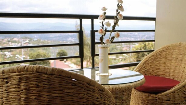 Wicker chairs with red cushions, a glass table, and a vase with flowers on a balcony overlooking a cityscape. - Apartment 6 - El Classico Apartments (Rubavu)