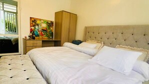 A bedroom with a large bed, a chest of drawers, a painting, and a window with bars. - Apartment 6 - El Classico Apartments (Rubavu)