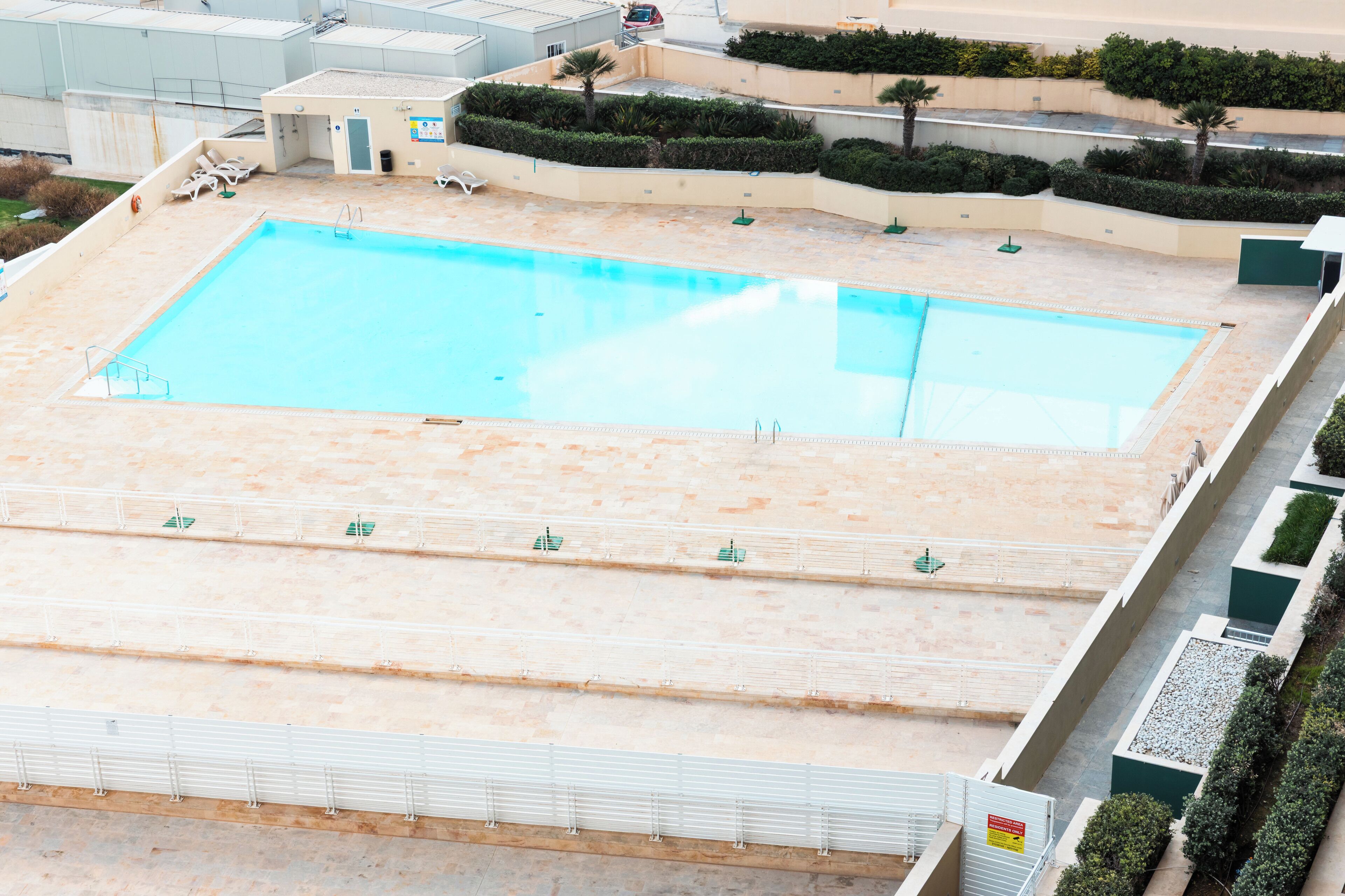A large rectangular swimming pool with a tiled deck area, surrounded by a low wall and a few lounge chairs.