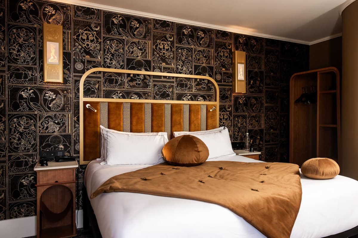 A bedroom with a large bed, a wooden headboard, and a patterned wallpaper.
