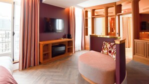 A hotel room with a television, a sofa, a small table, a window with curtains, and a view of the outside. - BOHEM Sacré Coeur (Paris)