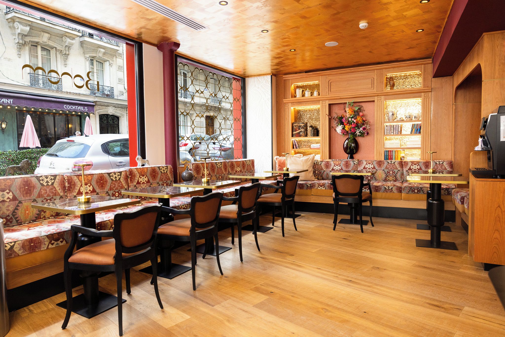 En restaurang med trägolv, möbler med mönstrat tyg och utsikt över gatan utanför.