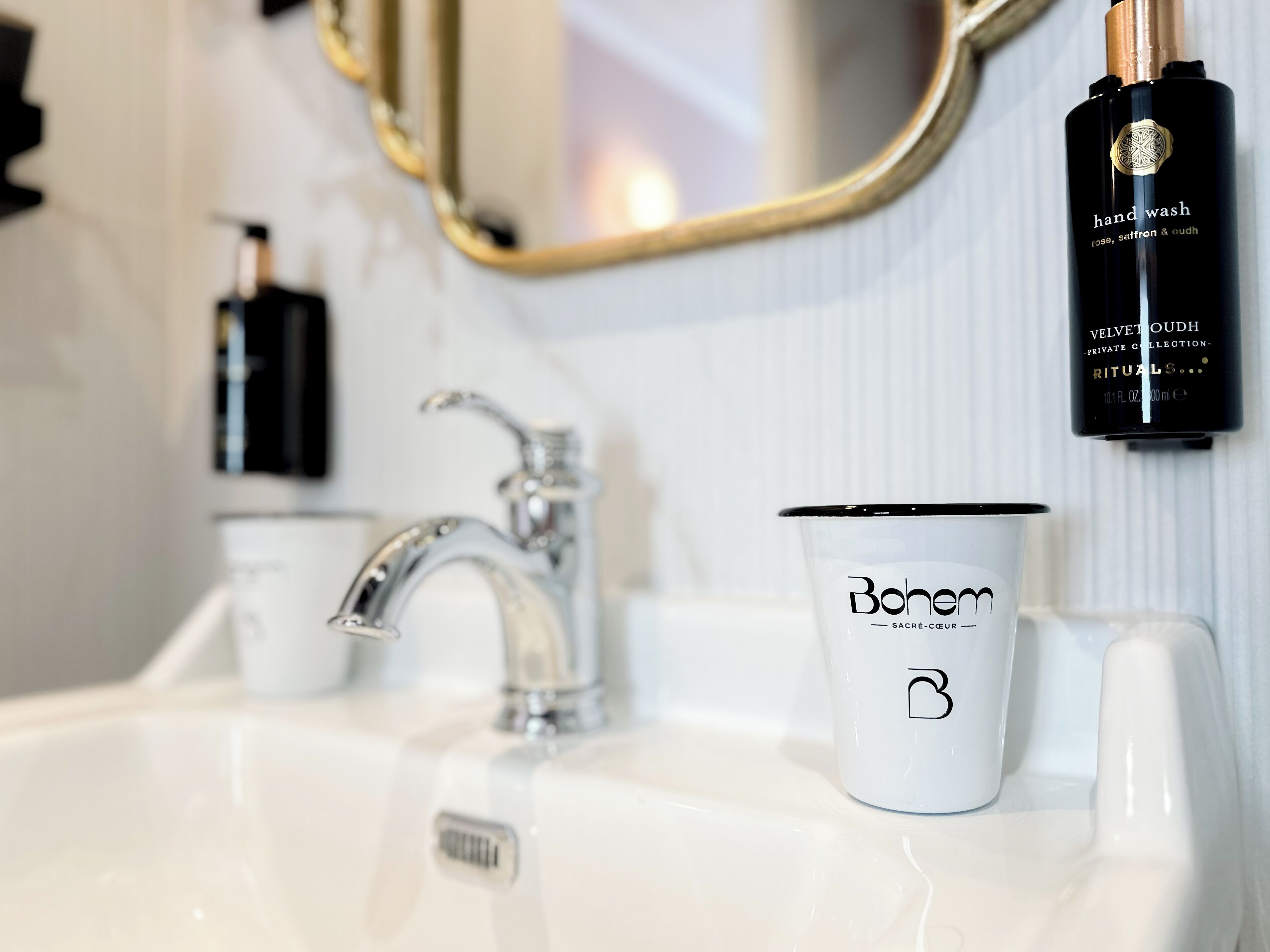 A bathroom with a white sink, a gold-framed mirror, and a Bohem branded cup.
