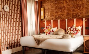 A hotel room with a patterned wall, a bed with multiple pillows, a nightstand, and a wall-mounted lamp. - BOHEM Sacré Coeur (Paris)