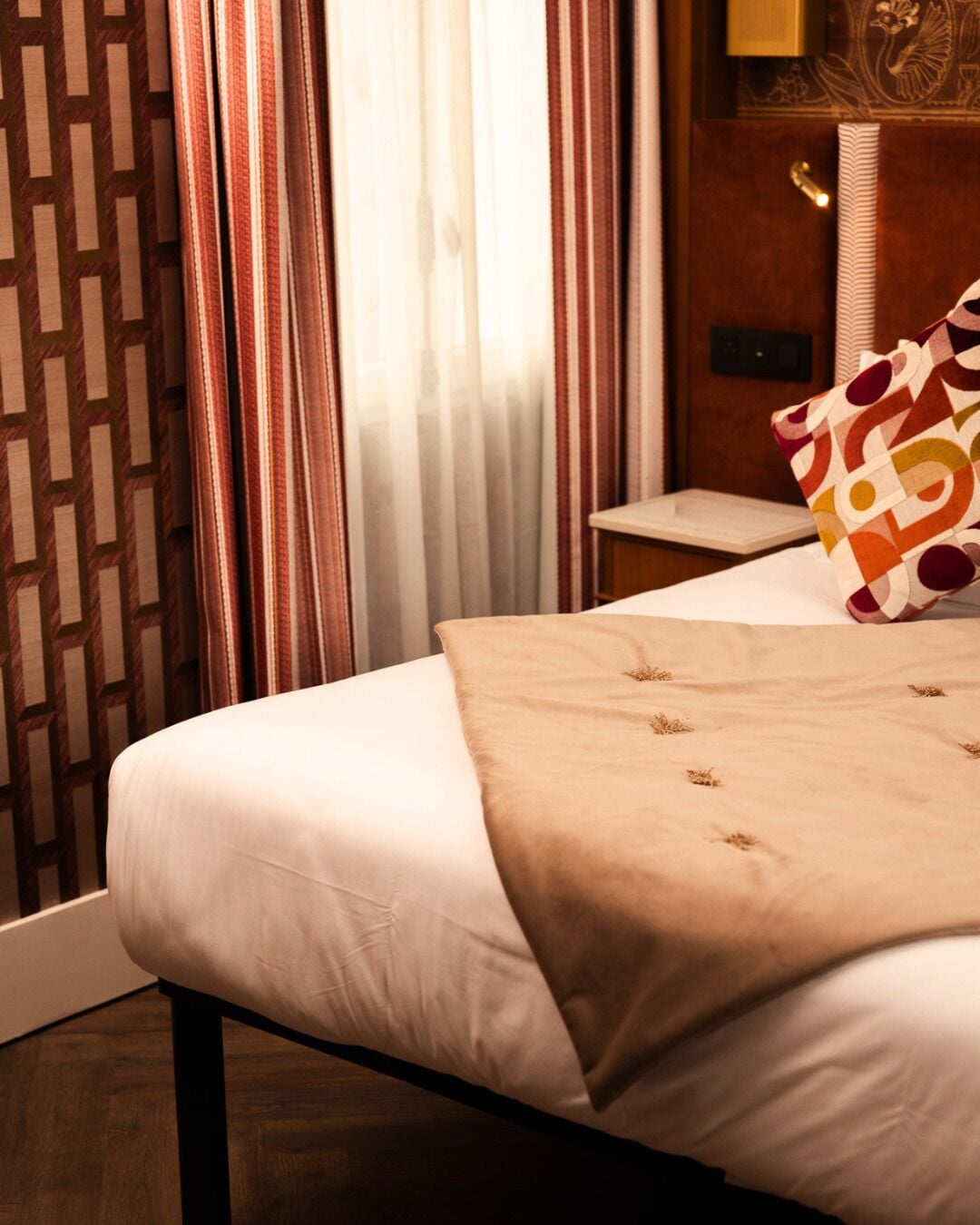 Una habitación de hotel con cama, mesita de noche, lámpara y cortinas.