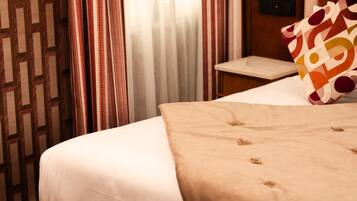Una habitación de hotel con cama, mesita de noche, lámpara y cortinas.