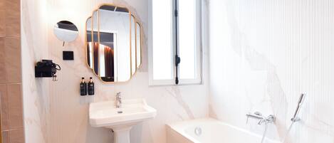 A bathroom with a bathtub, a sink, a mirror, and a window.