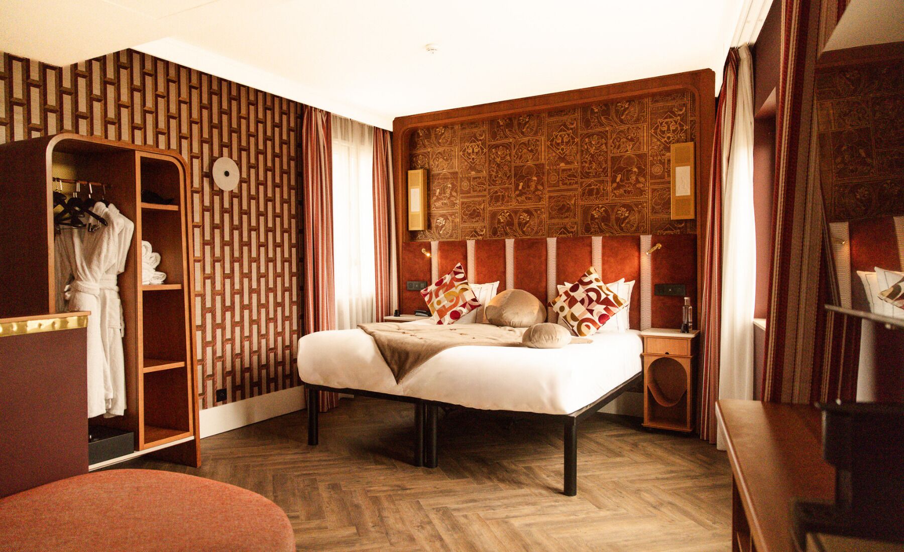 Habitación de hotel con cama, armario, espejo y suelo de madera.