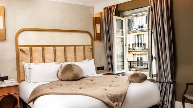 A hotel room with a bed, a bedside table, a chair, a window with curtains, and a view of a building. - BOHEM Sacré Coeur (Paris)