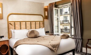 A hotel room with a bed, a bedside table, a chair, a window with curtains, and a view of a building. - BOHEM Sacré Coeur (Paris)
