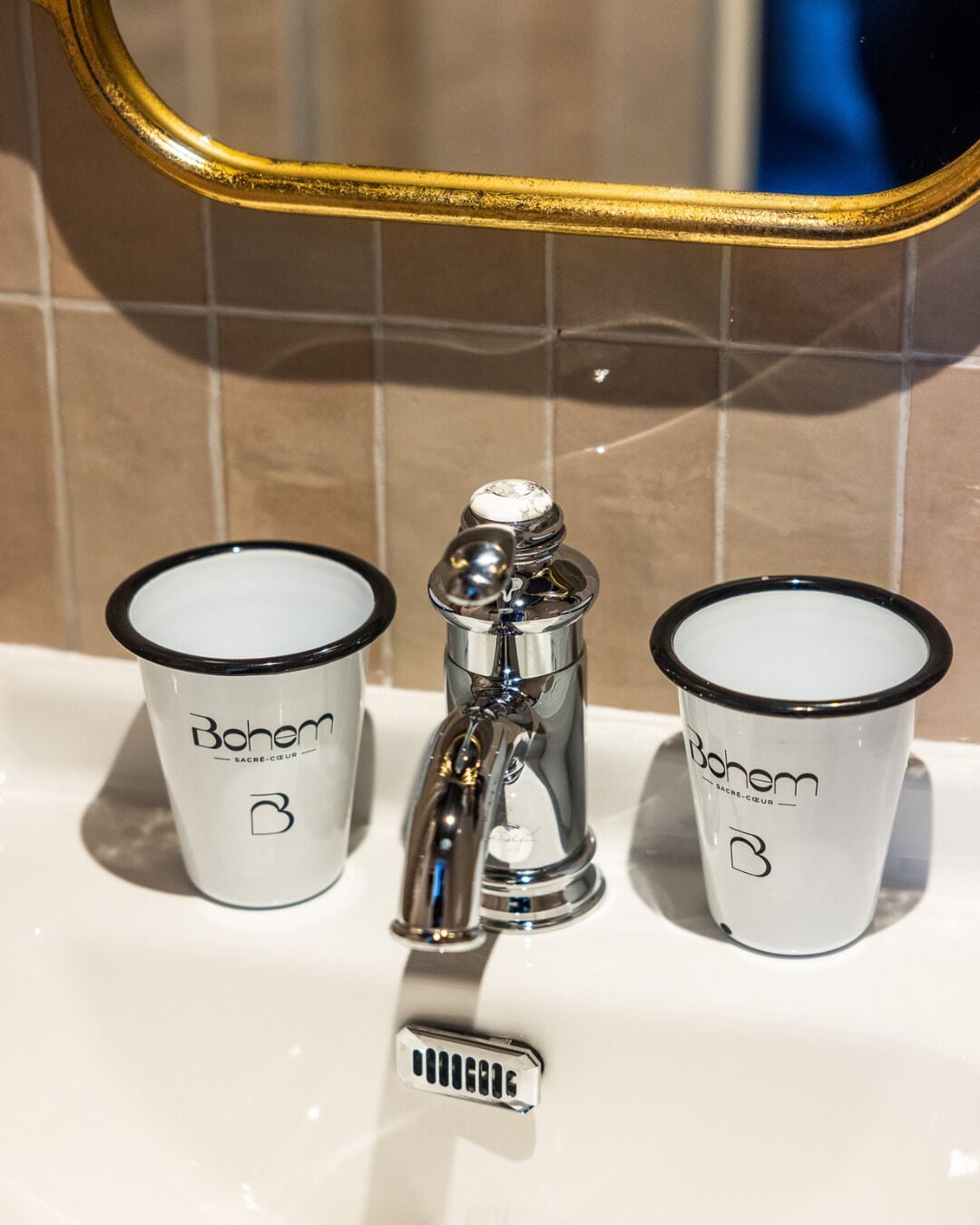A bathroom sink with two white cups labeled 'Bohem' and a chrome faucet.