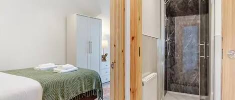 A bedroom with a bed, a wardrobe, and a shower area with a glass door.