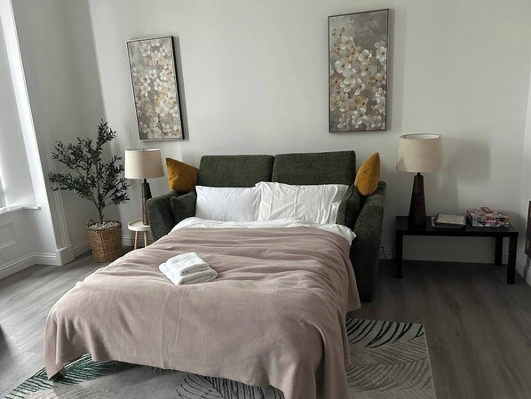 Une chambre à coucher moderne, avec un lit, deux tables de chevet, une lampe, une plante en pot et des œuvres d’art accrochées aux murs.