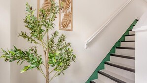 Een trap met witte treden en groene randen, een potplant met groene bladeren, en houten decoratie aan de muur.