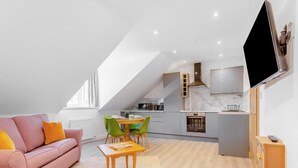 Een modern loft appartement met een eethoek, kitchenette en een grote televisie aan de muur.