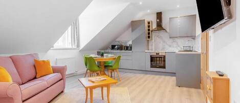 A modern loft apartment with a dining area, kitchenette, and a large TV mounted on the wall.