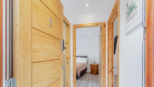Een hal met houten deuren, een bed, een nachtkastje en een aan de muur bevestigde televisie.