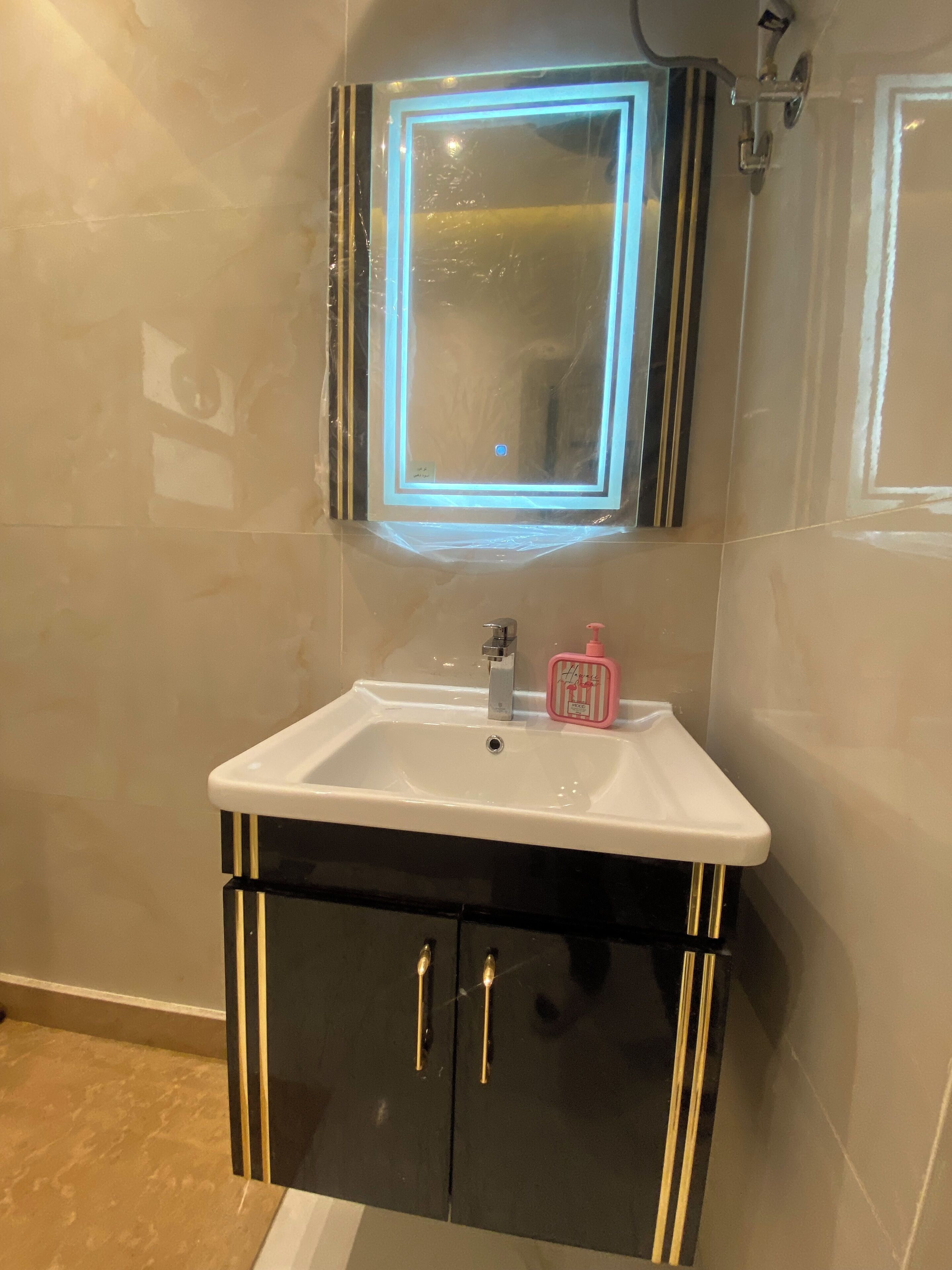 A bathroom with a white sink, black cabinet with gold handles, and a mirror with a blue light.