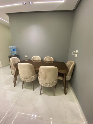 A dining area with a rectangular table and six chairs, a water dispenser, and a ceiling light fixture. - Spacious 3-bedroom apartment in soothing Hurghada with AC (Hurghada)
