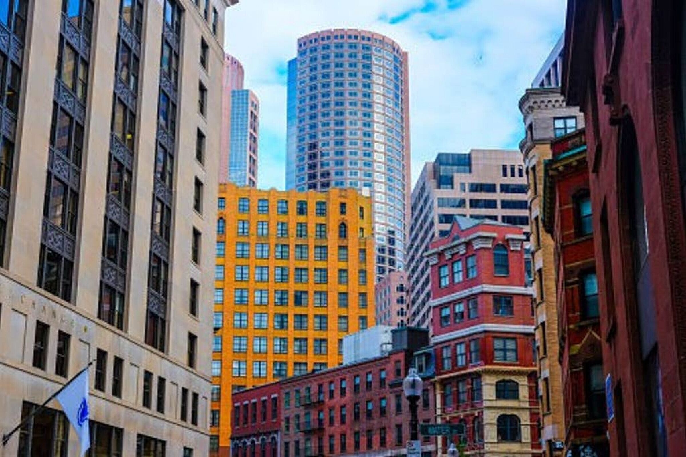 Un paisaje urbano con una variedad de estilos arquitectónicos, incluyendo un edificio amarillo destacado y un rascacielos azul alto.